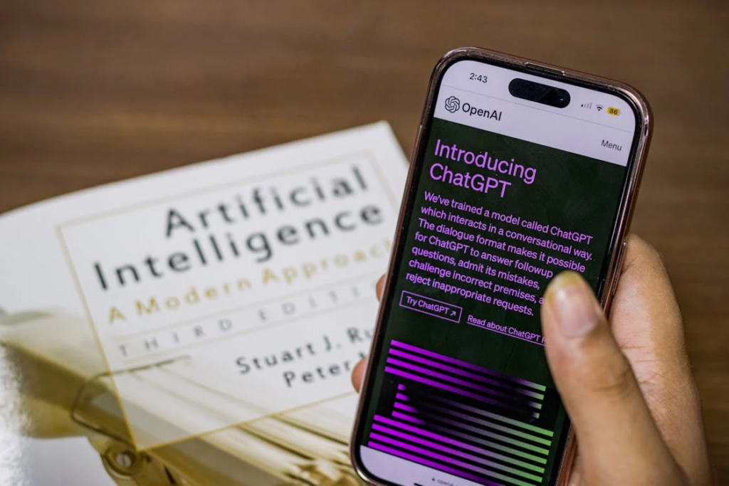 Person using ChatGPT on smartphone beside artificial intelligence book during career uncertainty.